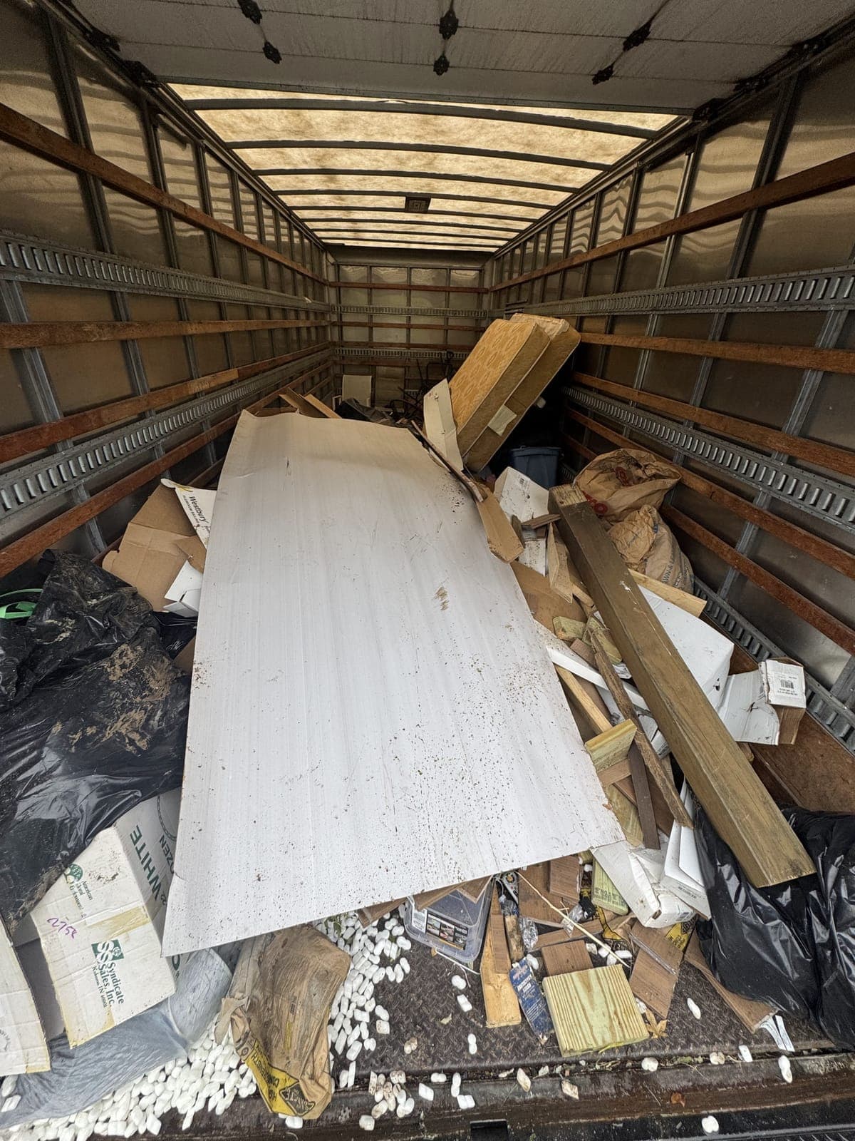 Inside a 26-foot box truck loaded with a large sheet panel, cut lumber, flattened cardboard, bagged debris and loose packing material on a mixed debris haul in the Kansas City metro