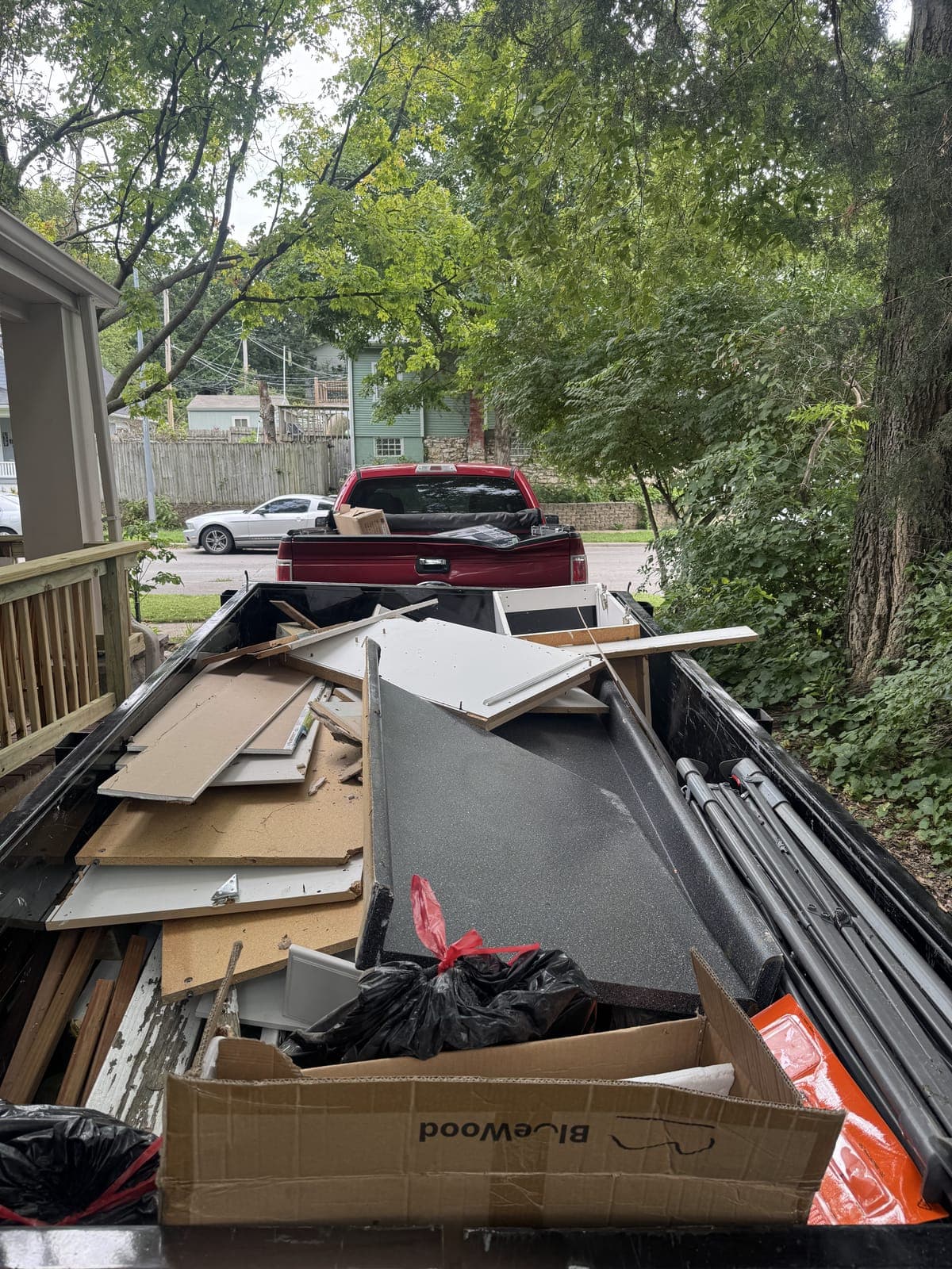 Dump trailer loaded beside a house with cabinet doors, particle board panels, a countertop section, and bagged debris from a kitchen remodel in the Kansas City metro
