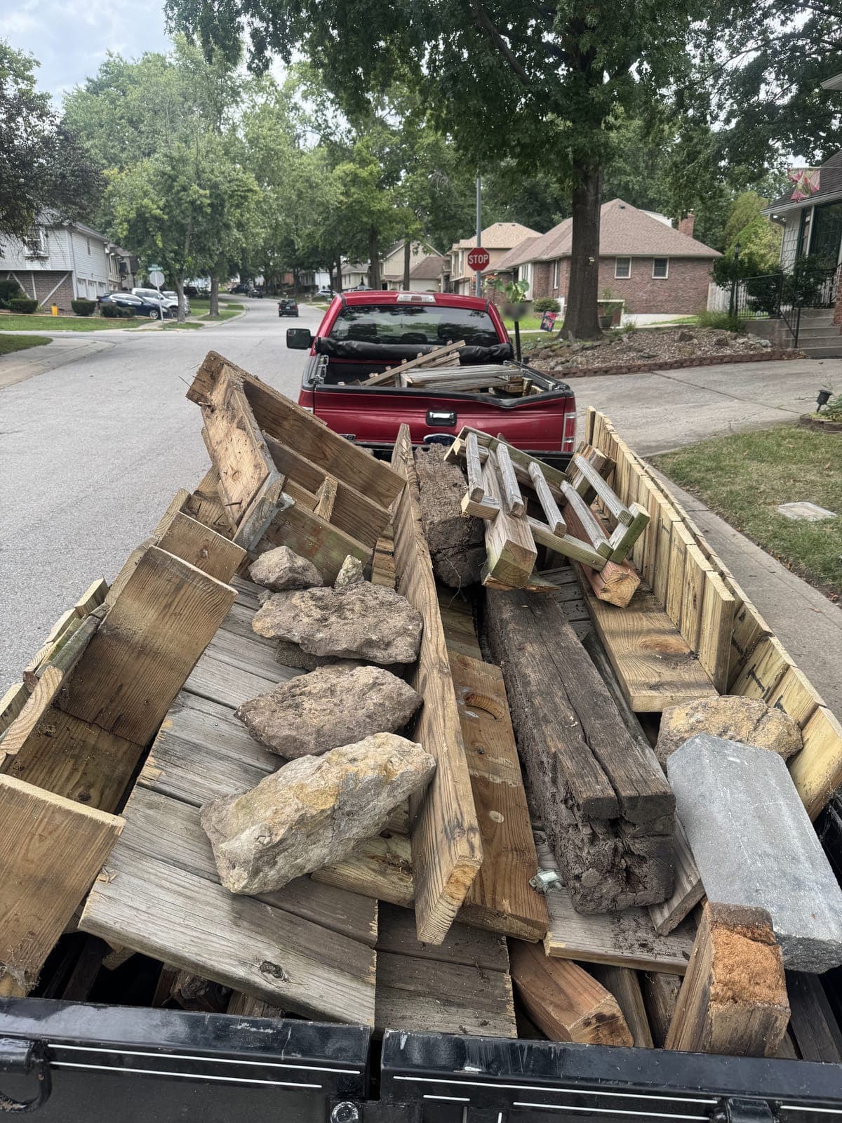 Dump trailer loaded curbside with torn-out deck lumber, railing sections, posts, and landscape stone on a deck teardown job in the Kansas City metro