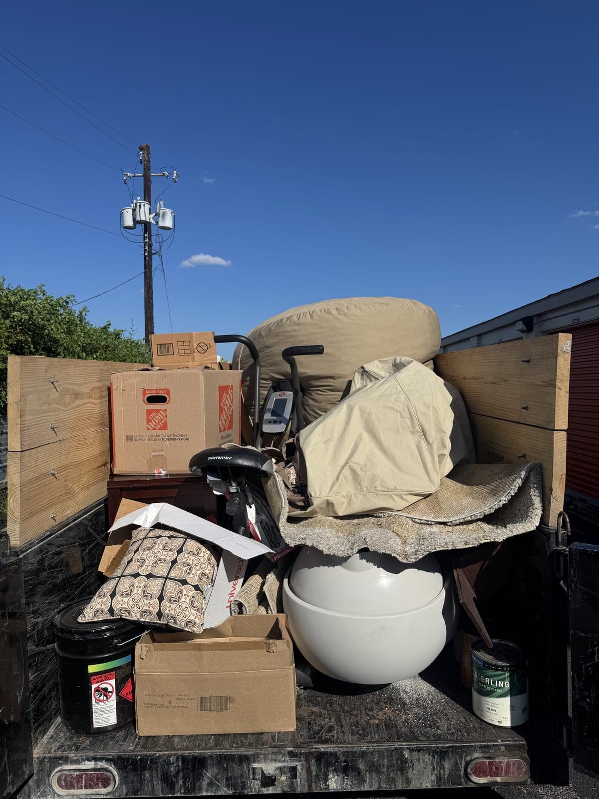Dump trailer with raised wood side extensions loaded with an exercise machine, a bicycle, moving boxes, a cushioned chair, rolled carpet padding, and a paint can on a household cleanout in the Kansas City metro