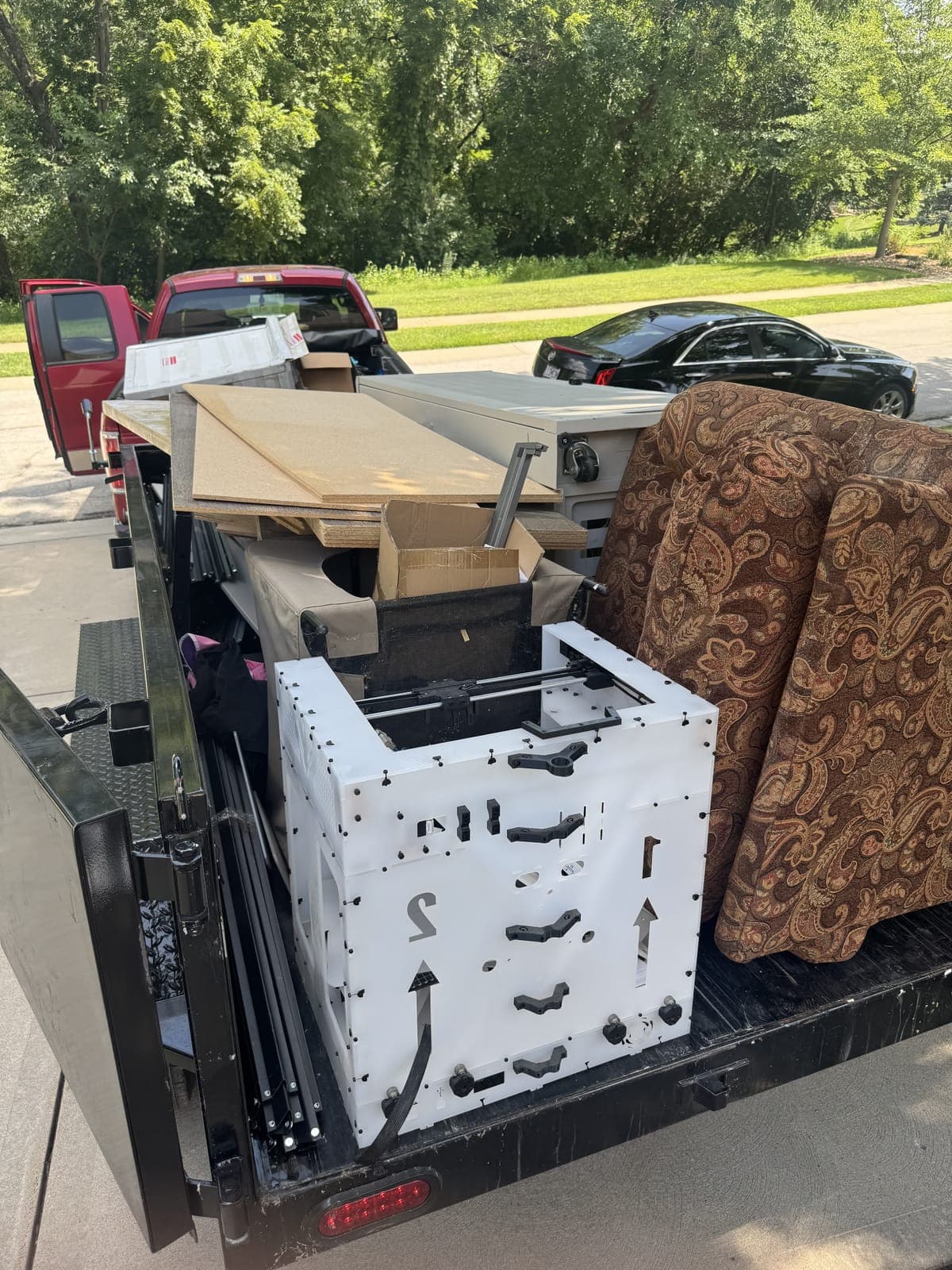 Dump trailer loaded curbside with an upholstered recliner, a cabinet, MDF shelving, and boxes on a residential furniture-removal job in the Kansas City metro