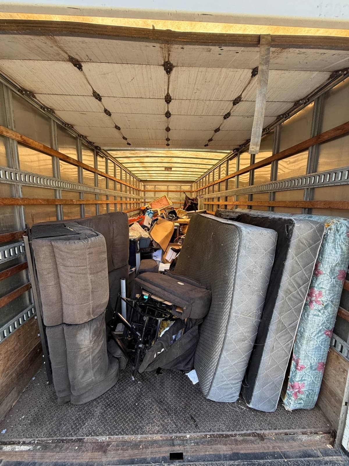 Interior of a 26-foot box truck packed with sectional sofa cushions, a folded recliner, four mattresses and box springs standing on edge, storage totes and cardboard boxes on a house cleanout in the Kansas City metro