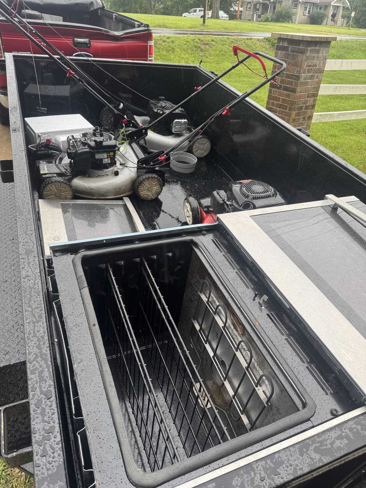 Dump trailer loaded with two push lawn mowers and an old oven range on a rainy-day appliance and yard-equipment haul in the Kansas City metro