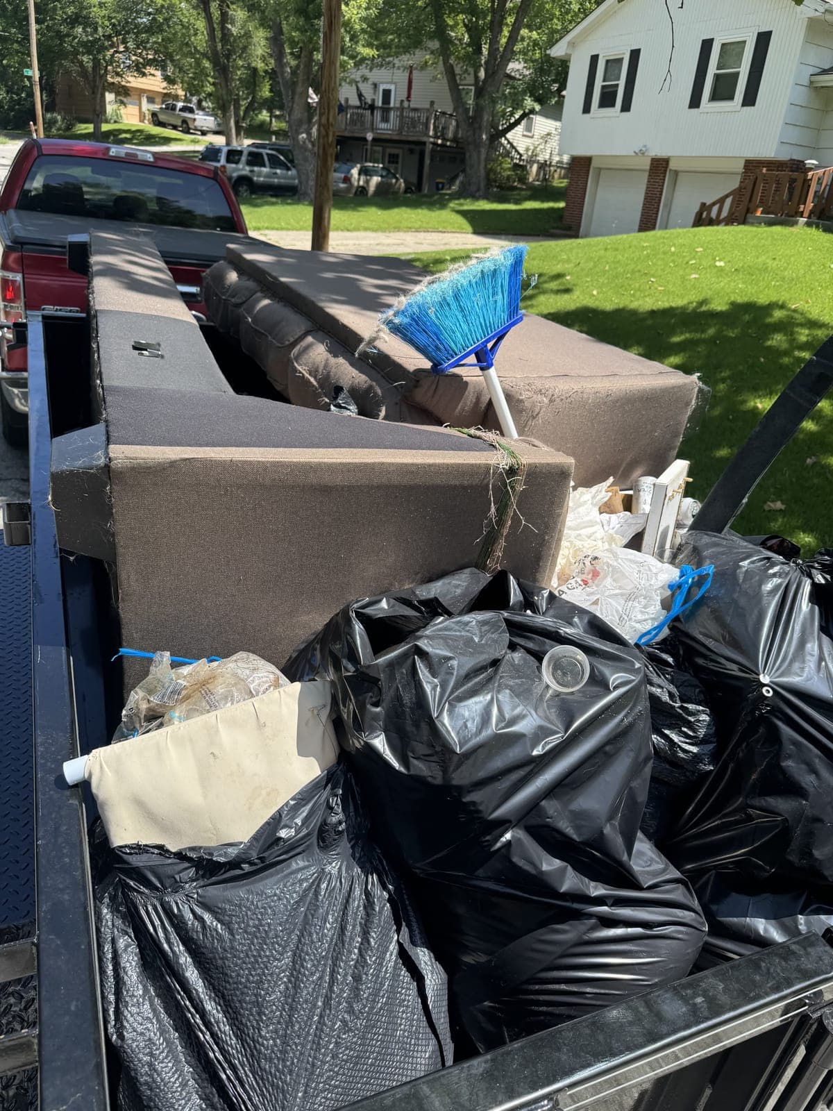 Dump trailer loaded curbside with an old brown sofa and bagged household junk on a furniture-removal job in Kansas City