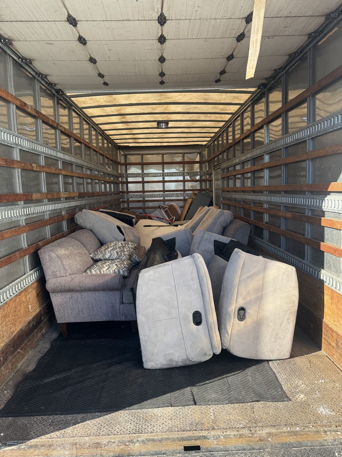 Inside a 26-foot box truck loaded with a gray fabric sofa and throw pillows, a gray reclining sectional taken apart into sections, and more household furniture on a furniture-removal job in the Kansas City metro