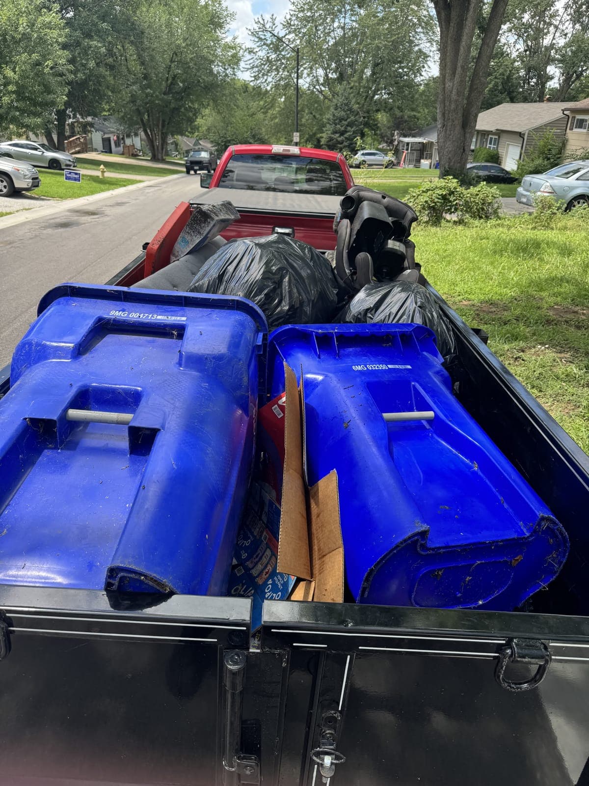 Dump trailer loaded with recycling bins, an office chair, and bagged household junk on a residential cleanout in the Kansas City metro
